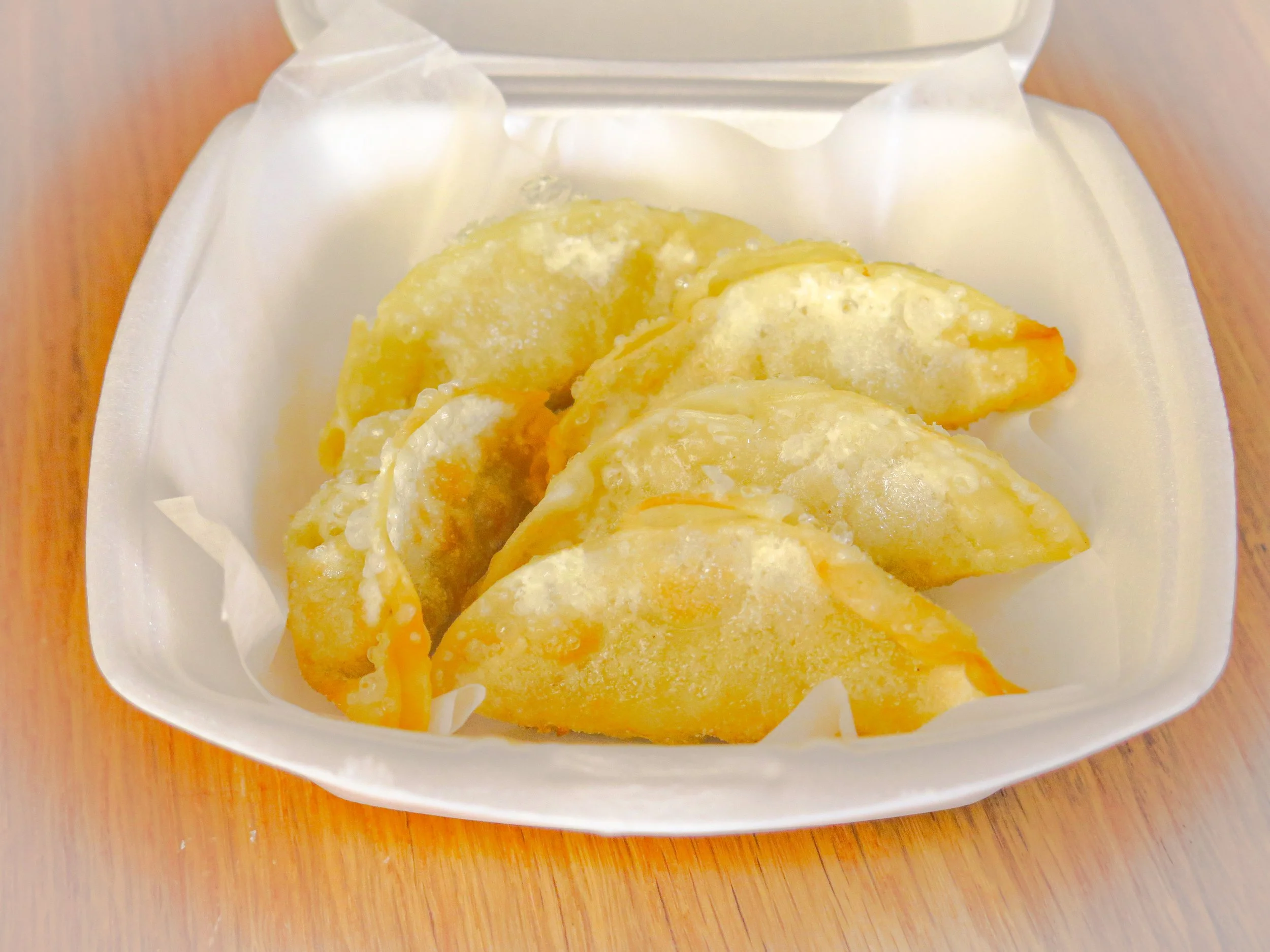 Six fried dumplings in a white foam takeout container
