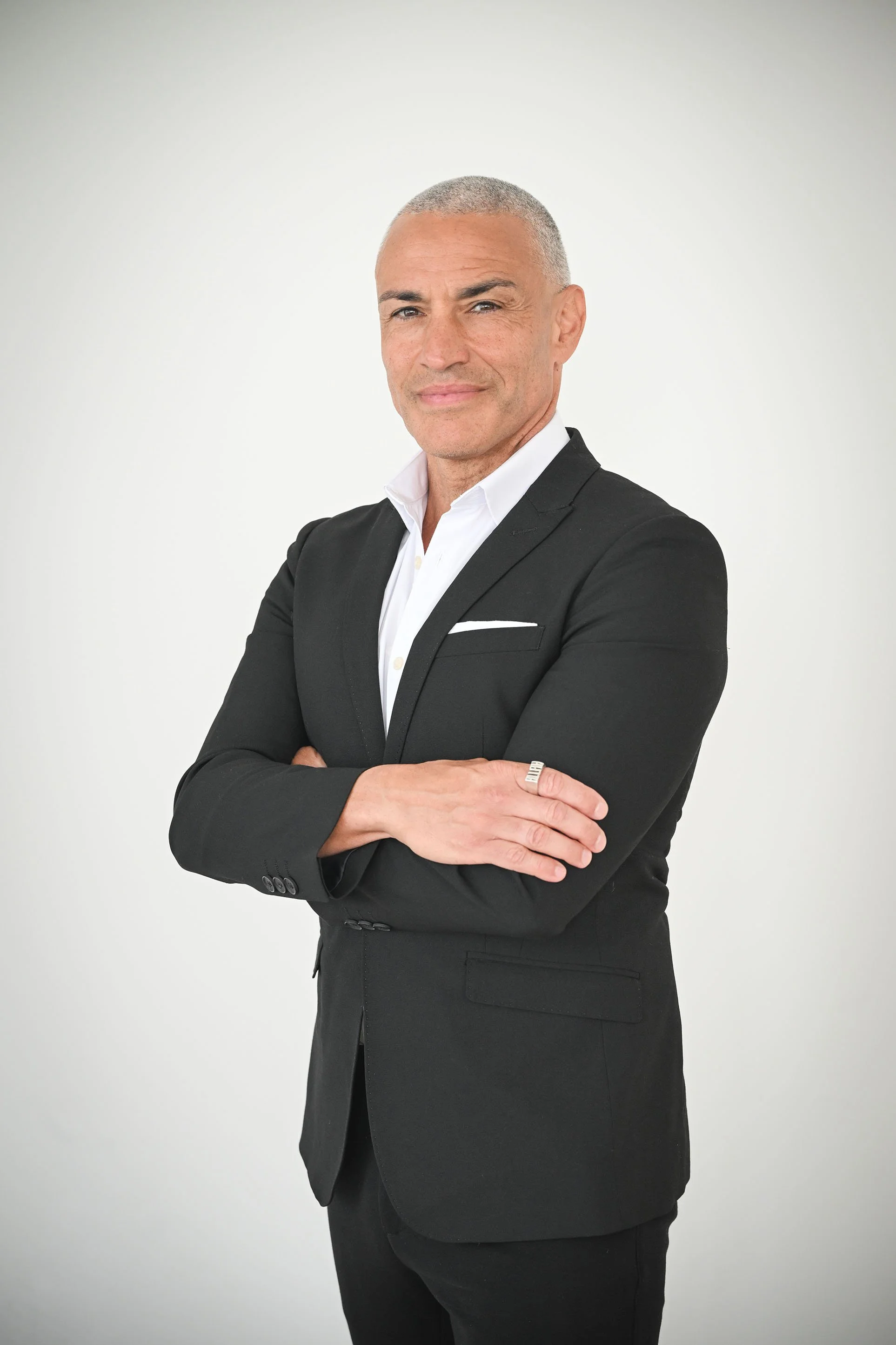 A professional man with gray hair in a black suit with arms crossed, standing against a plain white background.