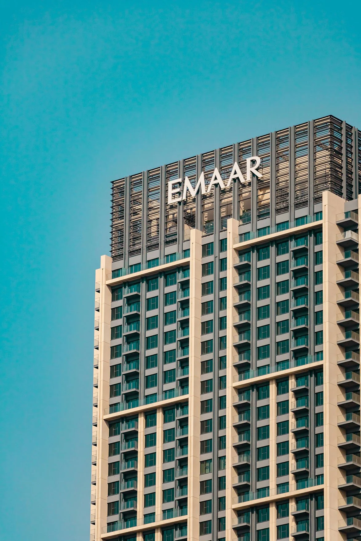 Tall modern skyscraper with the Emaar logo at the top against a clear blue sky.
