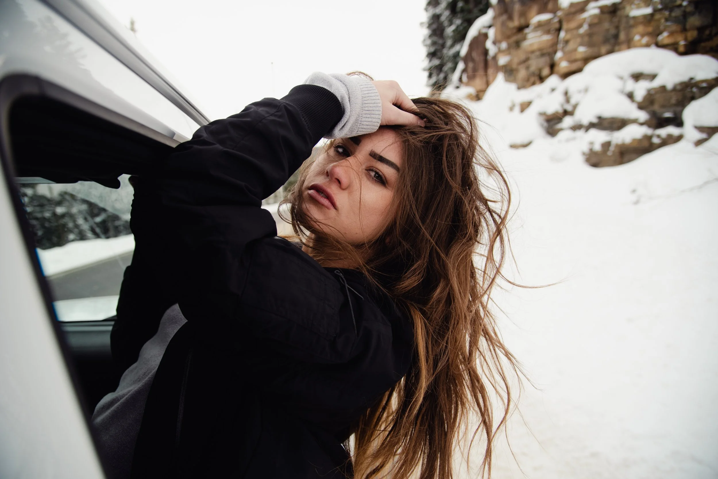 Woman with long hair leaning out of a car window in a snowy landscape.