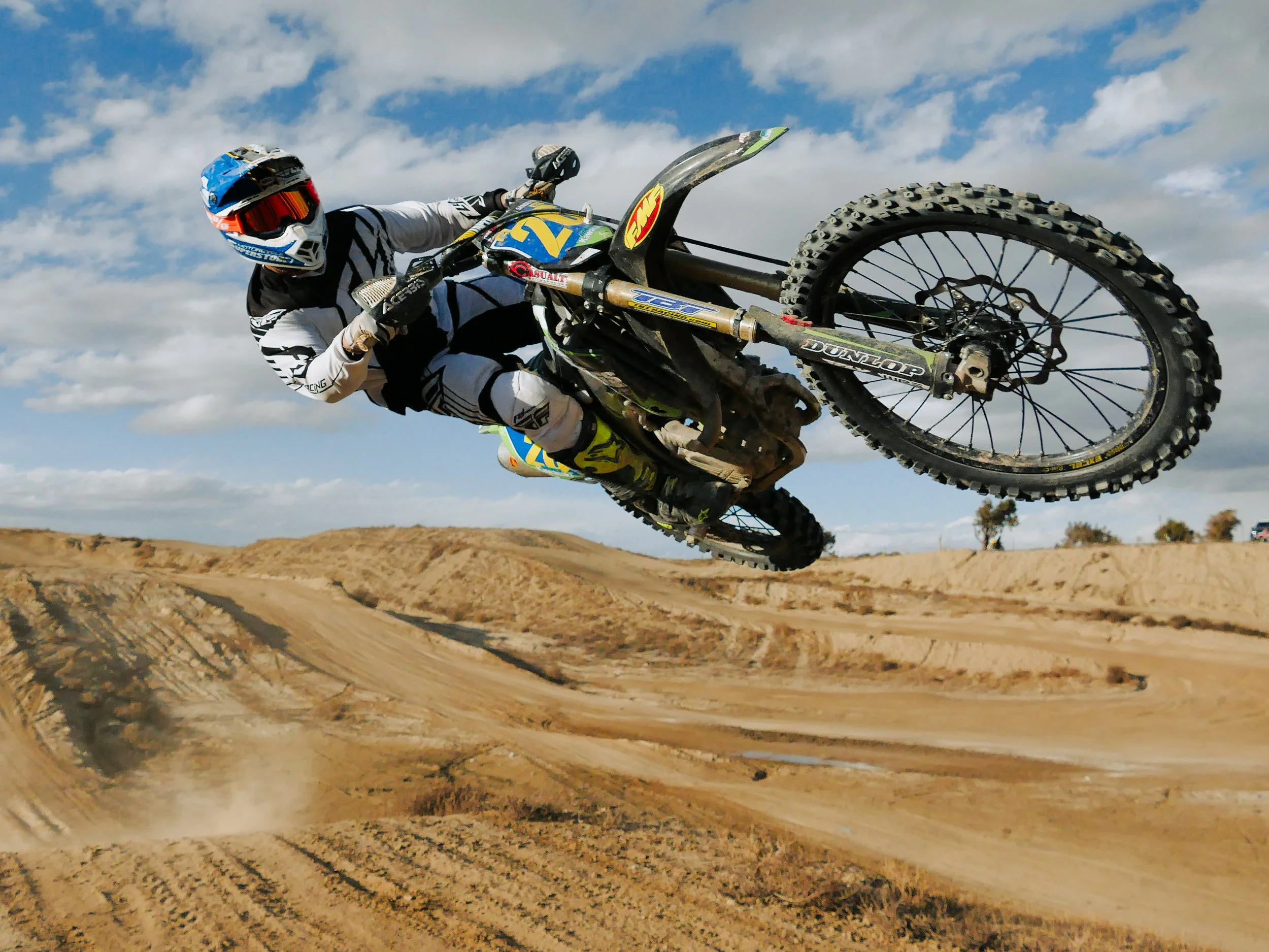 Motocross rider in white and black gear performing a jump on a dirt track with a clear sky background.