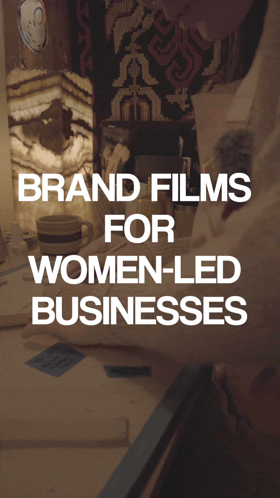 Text overlay on a photo that reads 'BRAND FILMS FOR WOMEN-LED BUSINESSES.' In the background, a cluttered desk or table with books, a mug, cards, and various objects, with a patterned rug or cloth on the wall.