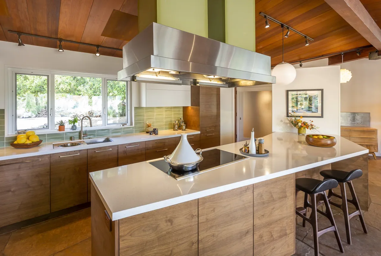 Topanga Canyon organic mid-century kitchen remodel with walnut cabinets, boomerang island, white stone countertop, green tile backsplash, wood ceiling, and original stainless steel hood.