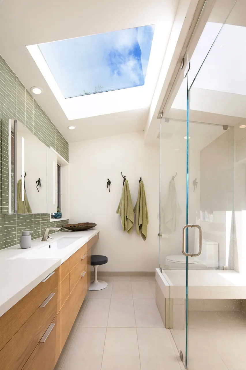 Organic mid-century modern primary bathroom remodel in Topanga Canyon featuring skylight, floating walnut vanity, green tile accent wall, and frameless glass shower enclosure.