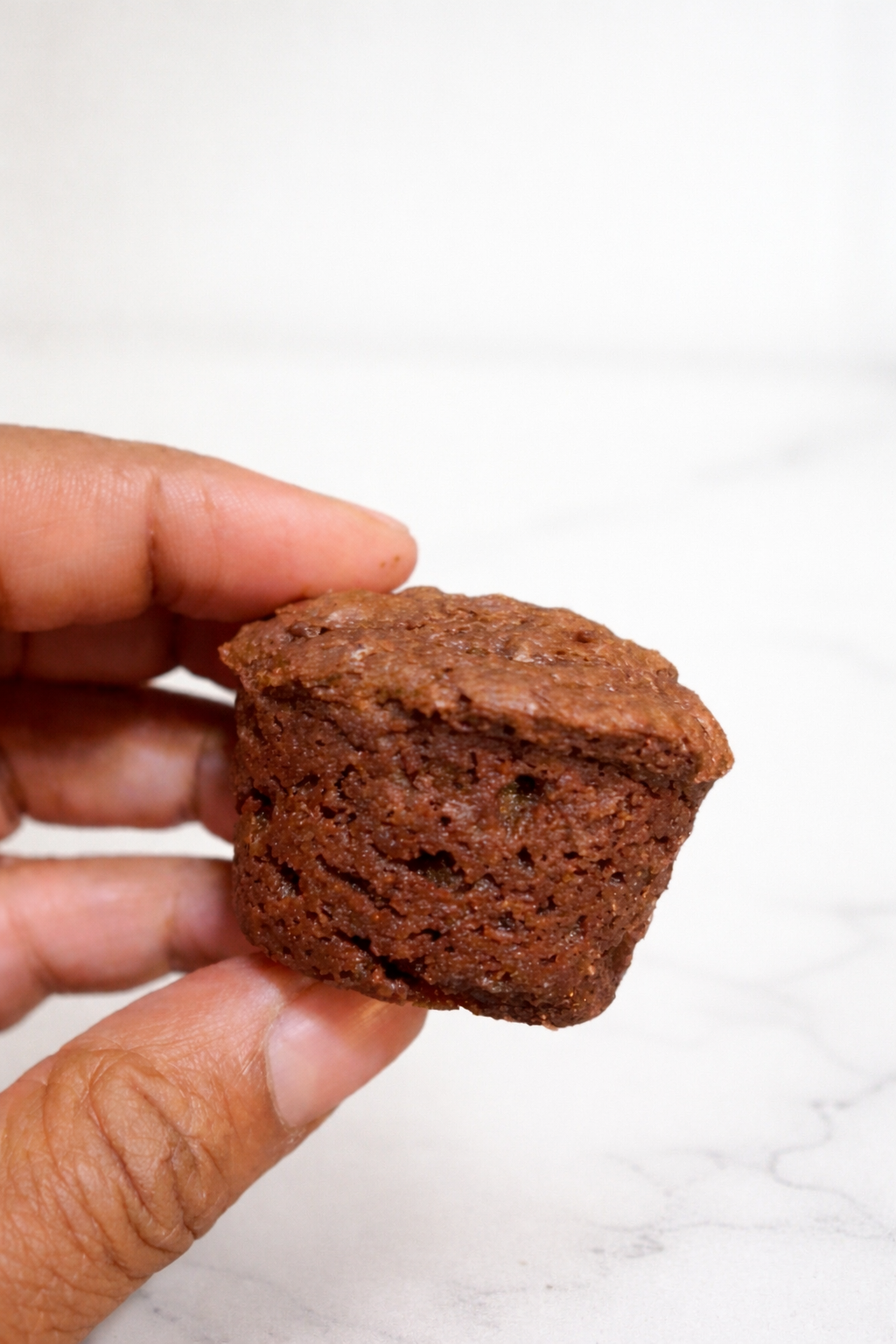 Hand holding a brownie bite with a white background.