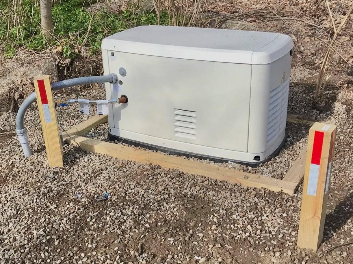 A refrigerator installed outdoors on a gravel surface, surrounded by wooden blocks and stakes, with tubing connected to it.