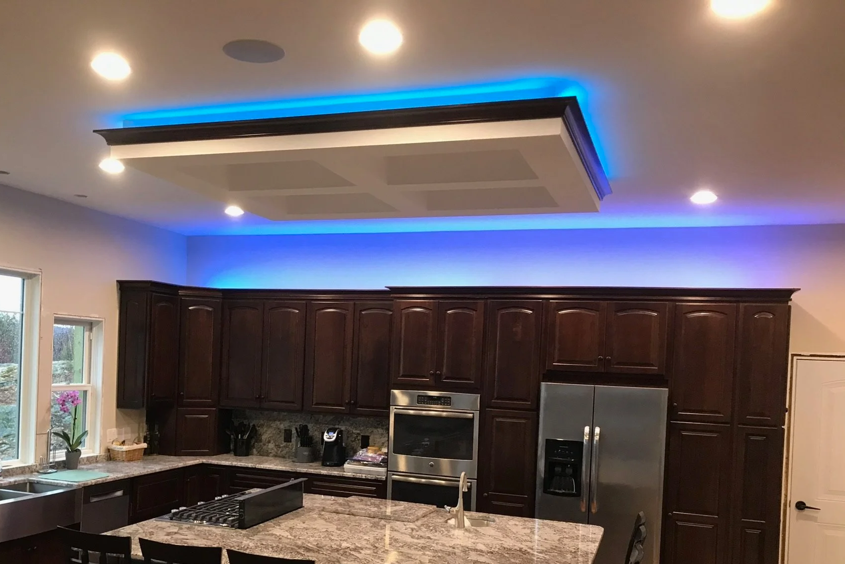 Modern kitchen with dark wood cabinets, granite countertops, stainless steel appliances, and a ceiling feature with blue LED lighting.