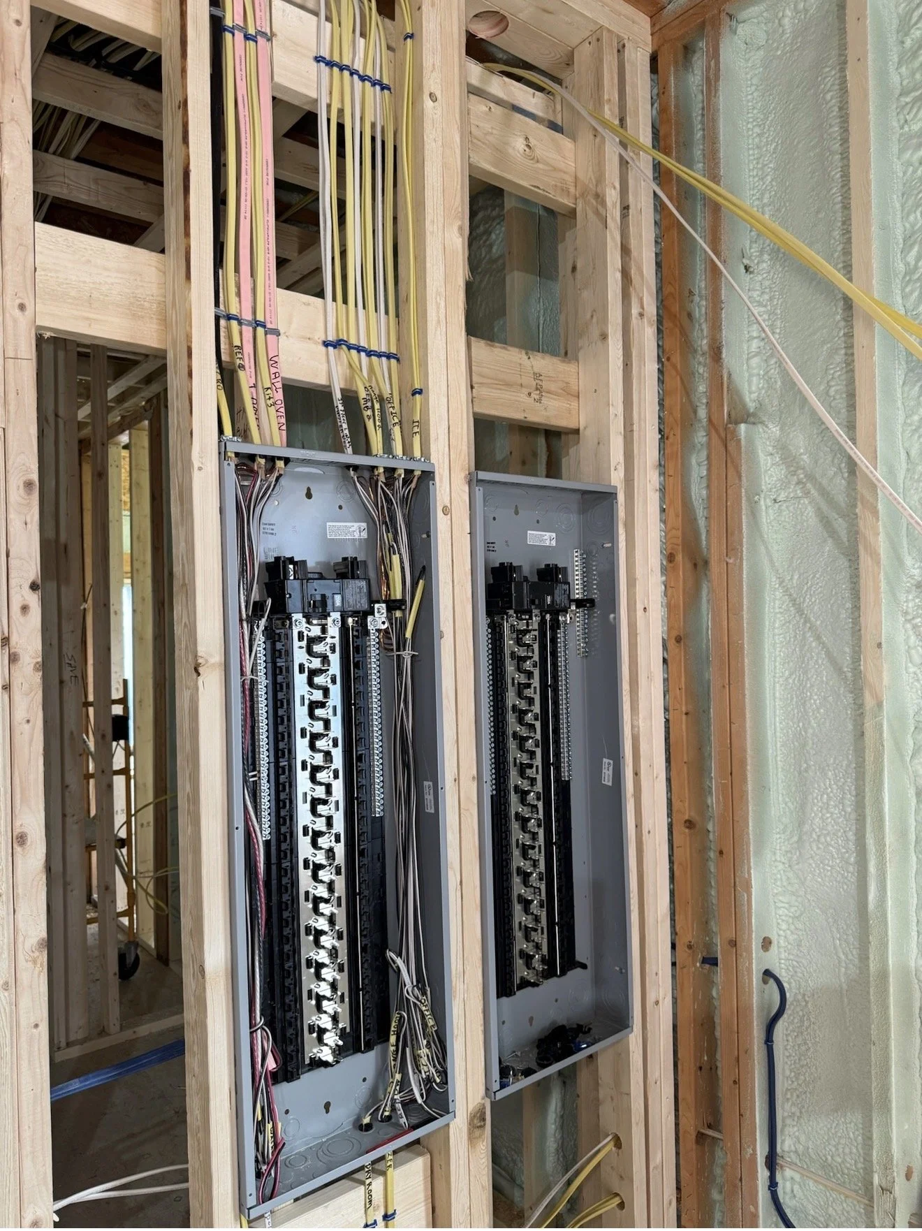 Electrical wiring and circuit breaker panels installed in a wooden framing wall under construction.