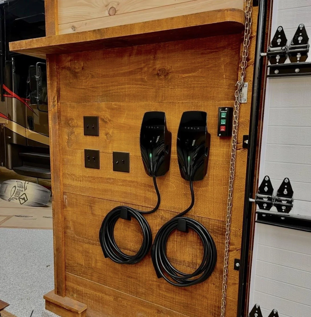 Wall-mounted Tesla electric vehicle chargers with power cords, electrical outlets, and a control panel on a wooden wall.
