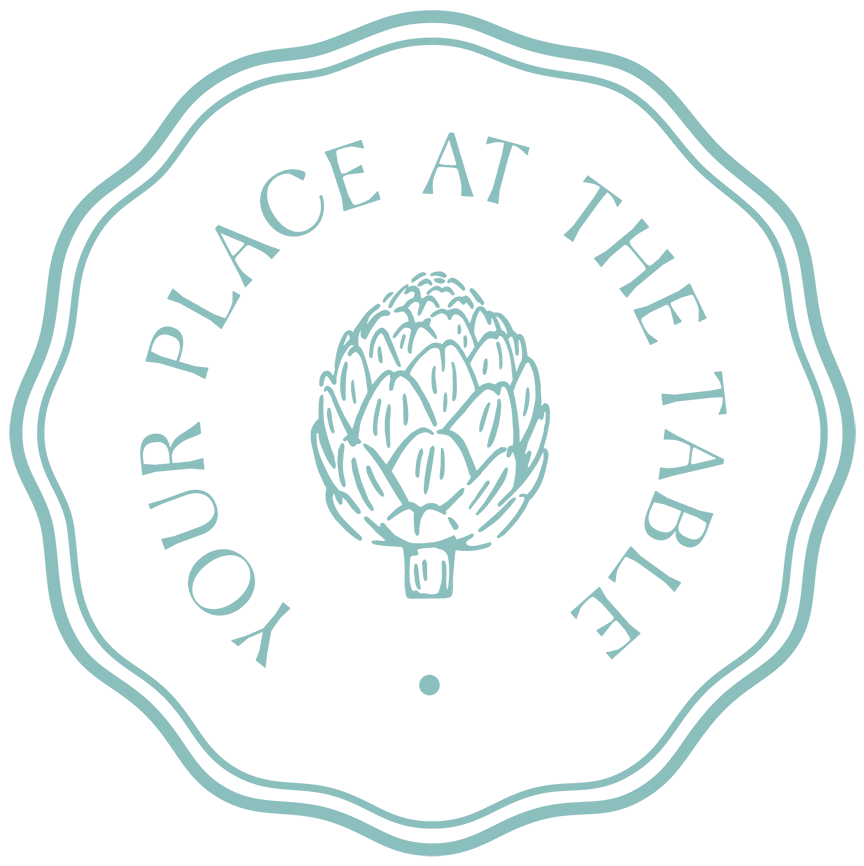 A fluted circular logo with a light blue-green border and text that says 'Your Place at the Table' encircling a central illustration of an artichoke.