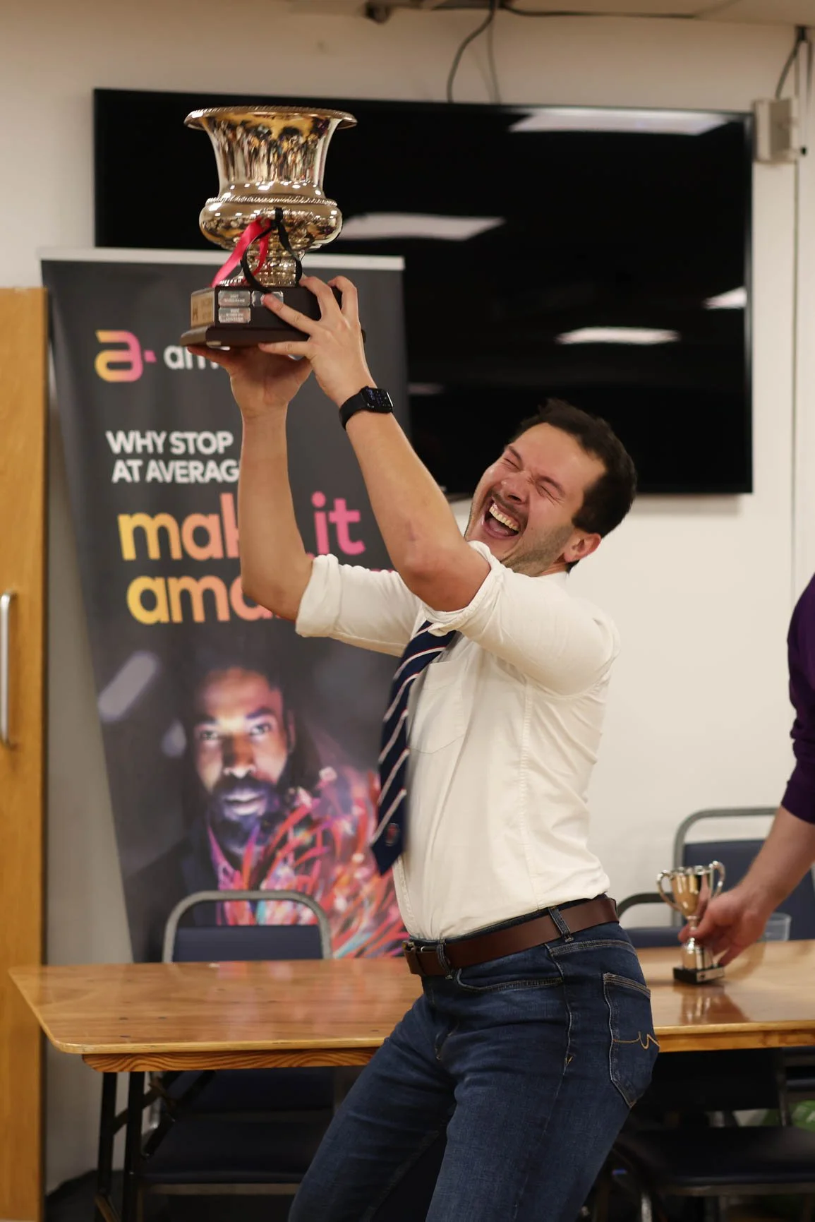 A man is smiling and celebrating while holding a trophy above his head at an award ceremony.
