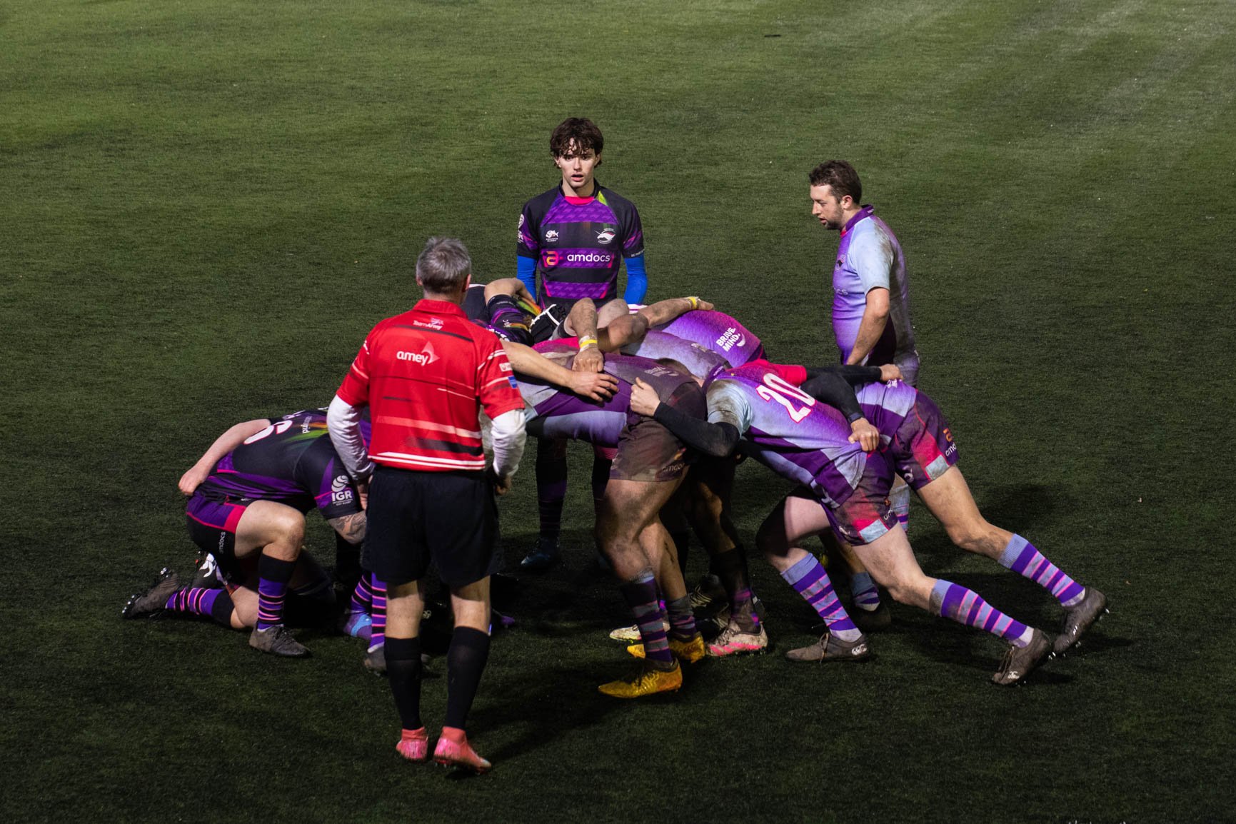 Rugby players engaged in a scrum on the field, with officials observing.