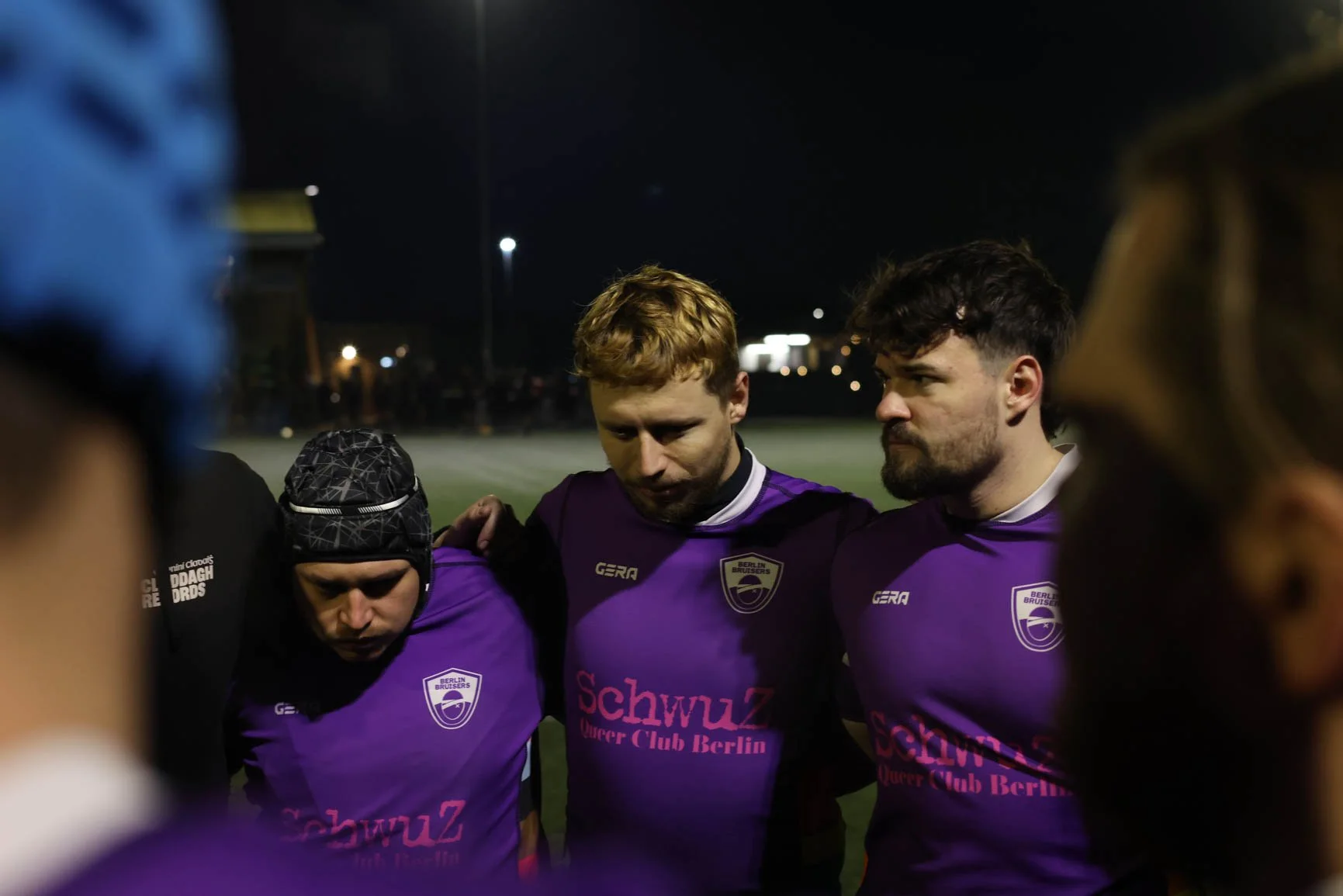 A group of soccer players wearing purple jerseys with the Berlin Braves logo, standing together in a circle during a night game.