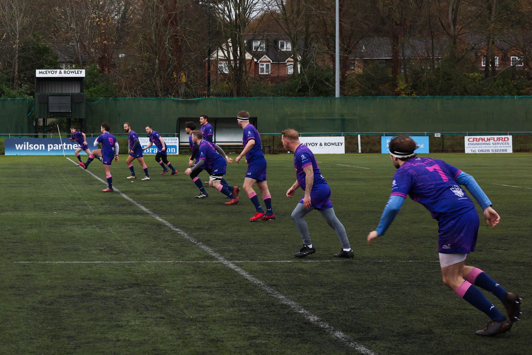 A rugby team in purple uniforms doing warm-up exercises on a rugby field.