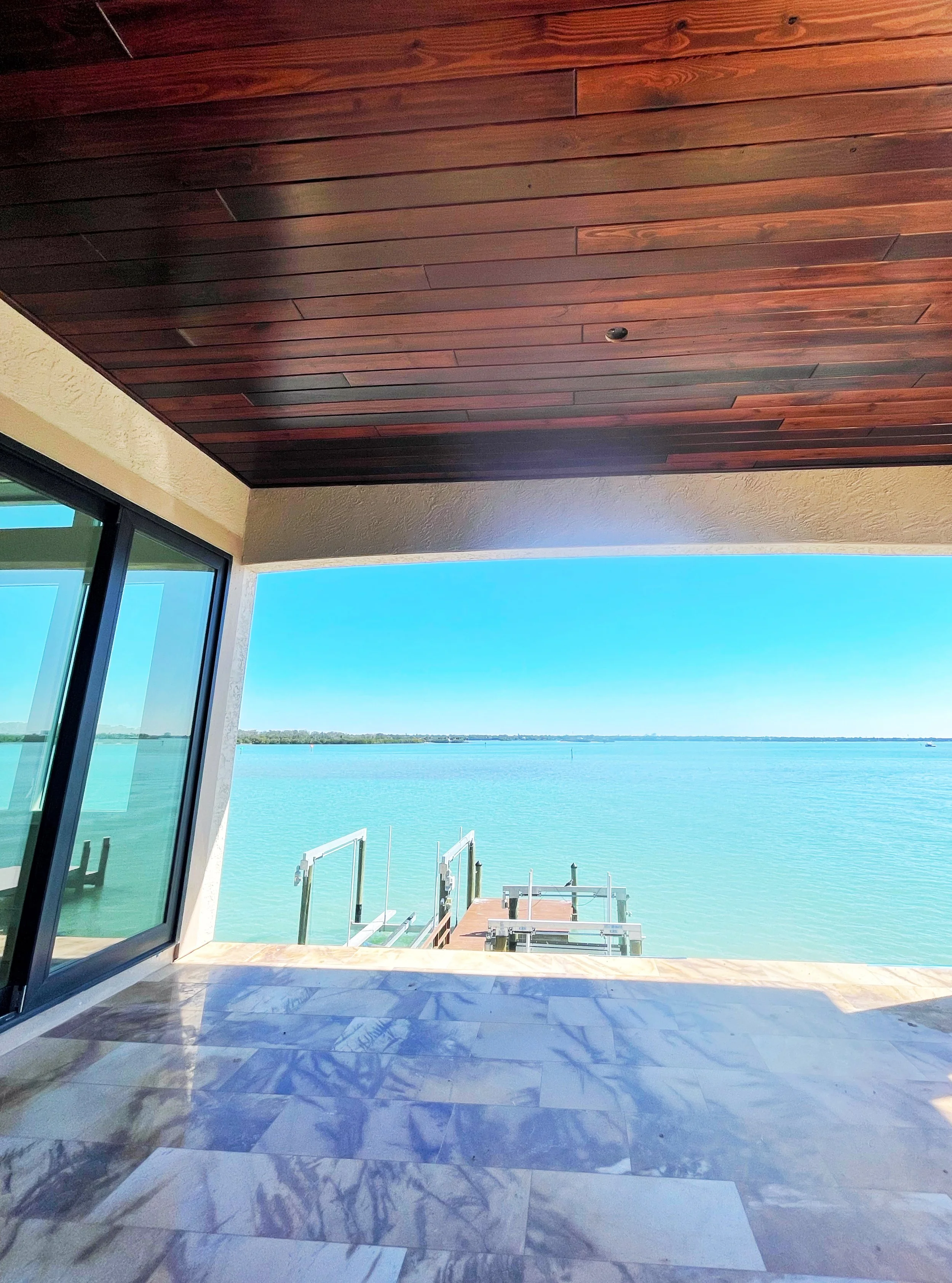 Balcony with marble flooring, a two-tone wood ceiling, and a sliding glass door.