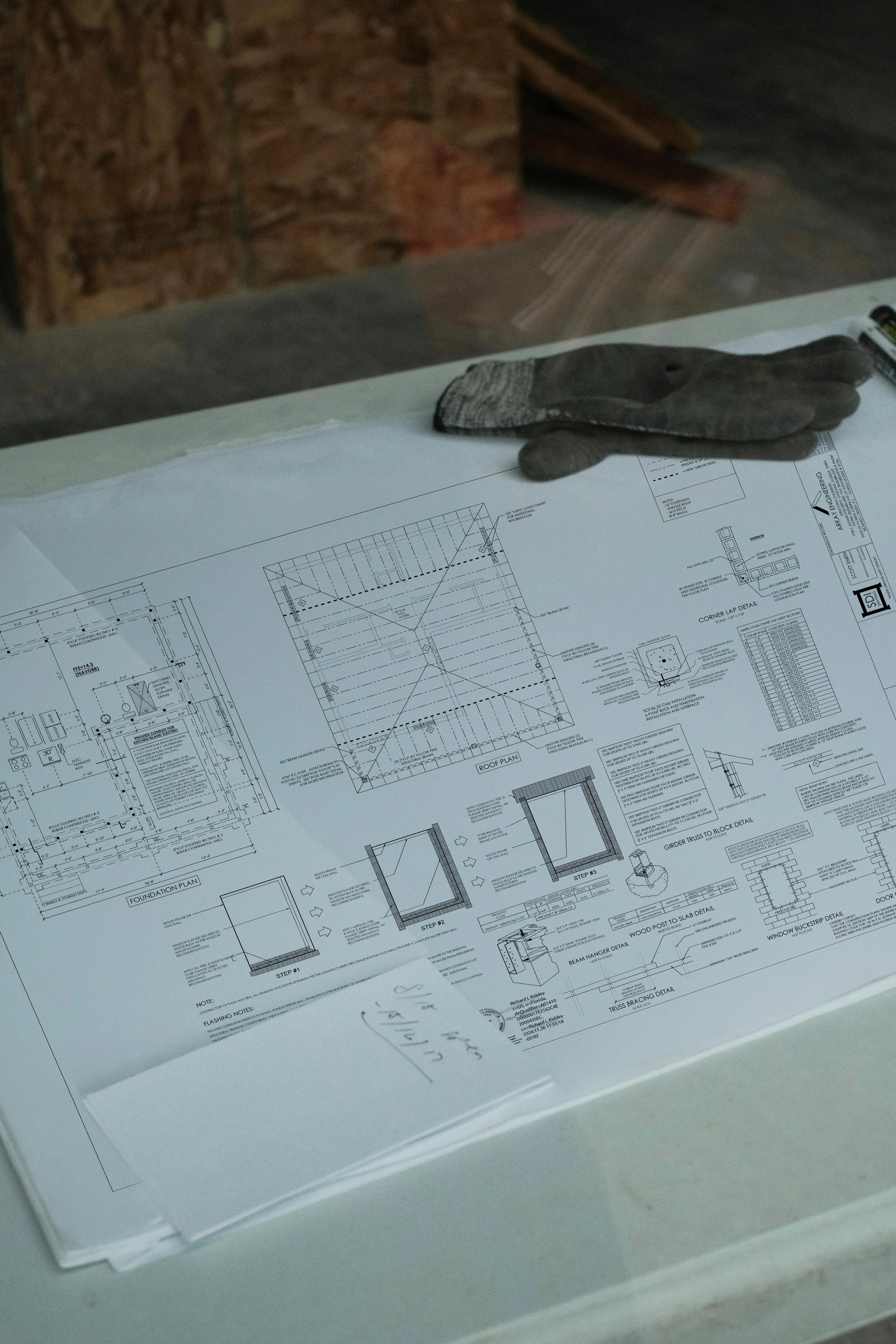 Blueprints and construction plans on a table with gloves placed on top. Site Coordination.