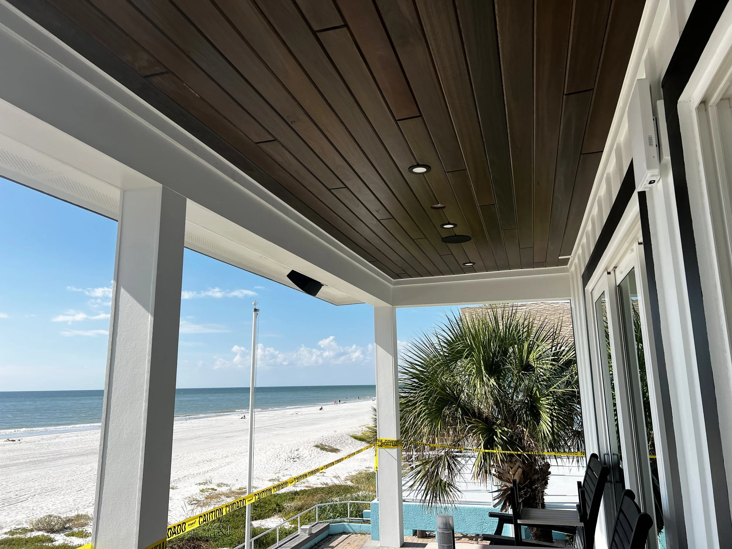 A beachside patio with a wooden ceiling, white support beams, and sliding glass doors.