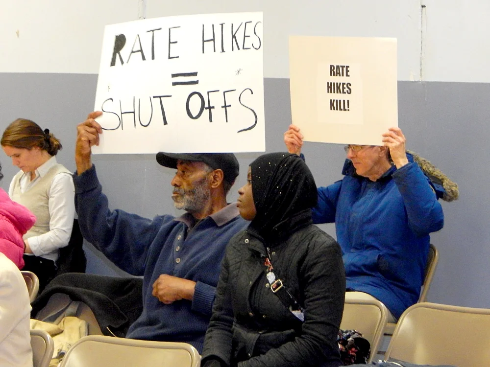 ESWA members at utility hearing hold up signs saying "rate hikes equal shut-offs" and "rate hikes kill"