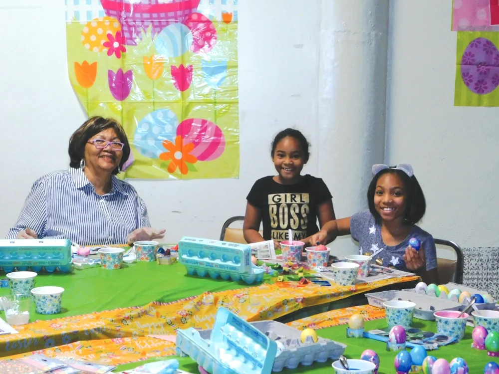 A member supervises two smiling girls coloring and decorating eggs at the Spring Family Celebration