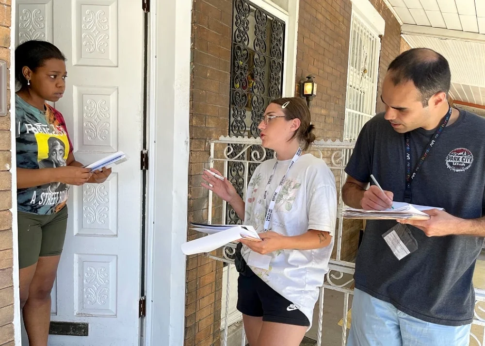 A canvass team of 2 volunteers sign up a member at her doorway. 