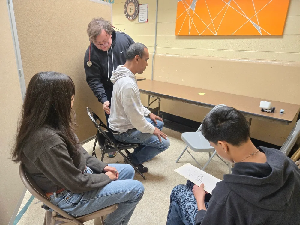 A volunteer physician does a check up for a member at a General Medical Session with a volunteer advocate making notes for follow-up care