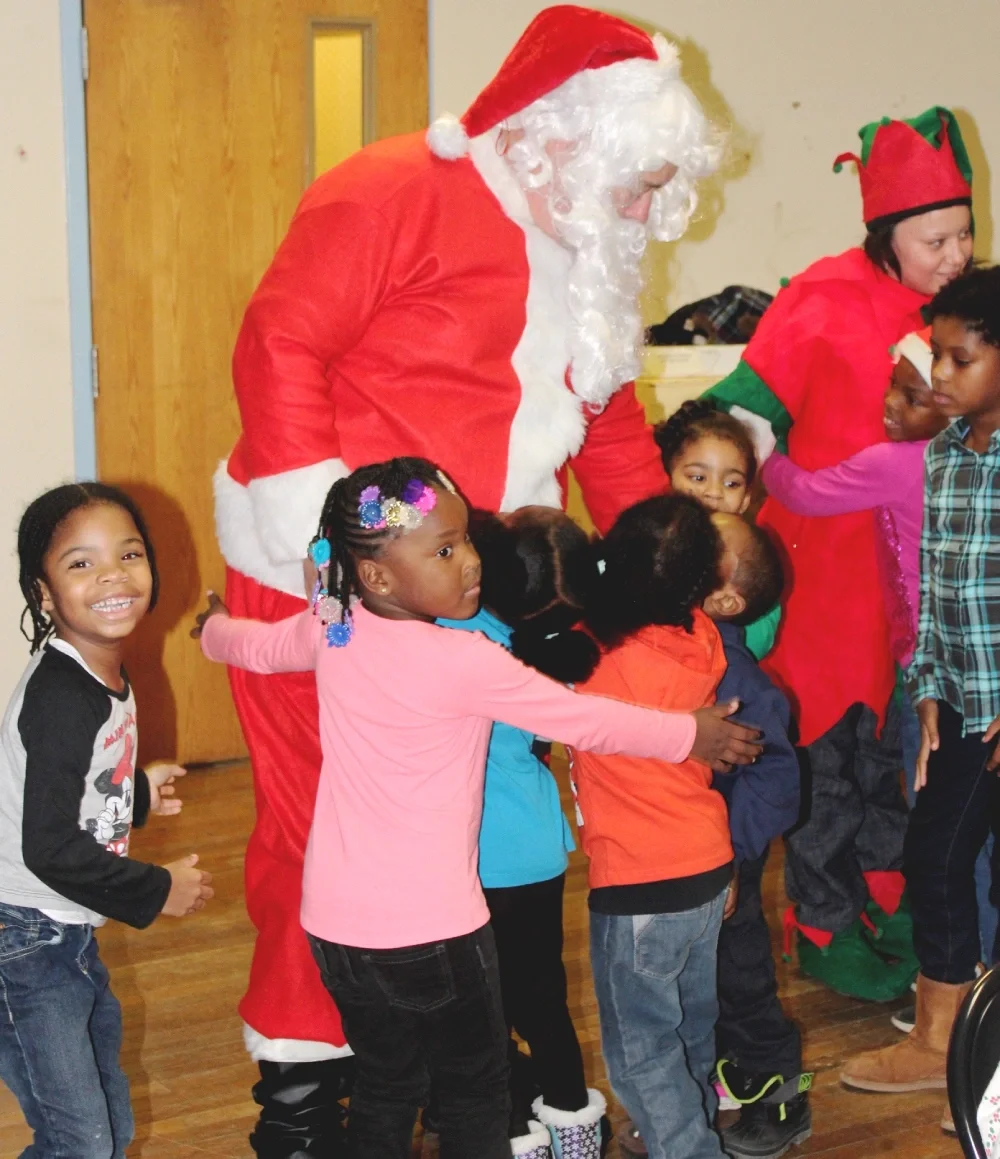 Children gather around to hug Santa Claus at the Holiday Family Party