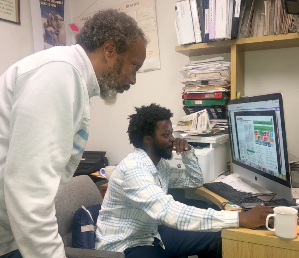 Two volunteers work on the computer to assemble the next issue of ESWA's Philadelphia Service Worker newspaper
