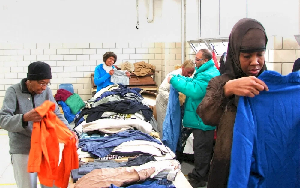 A group of members sorting and selecting clothing from a long table with clothing laid out