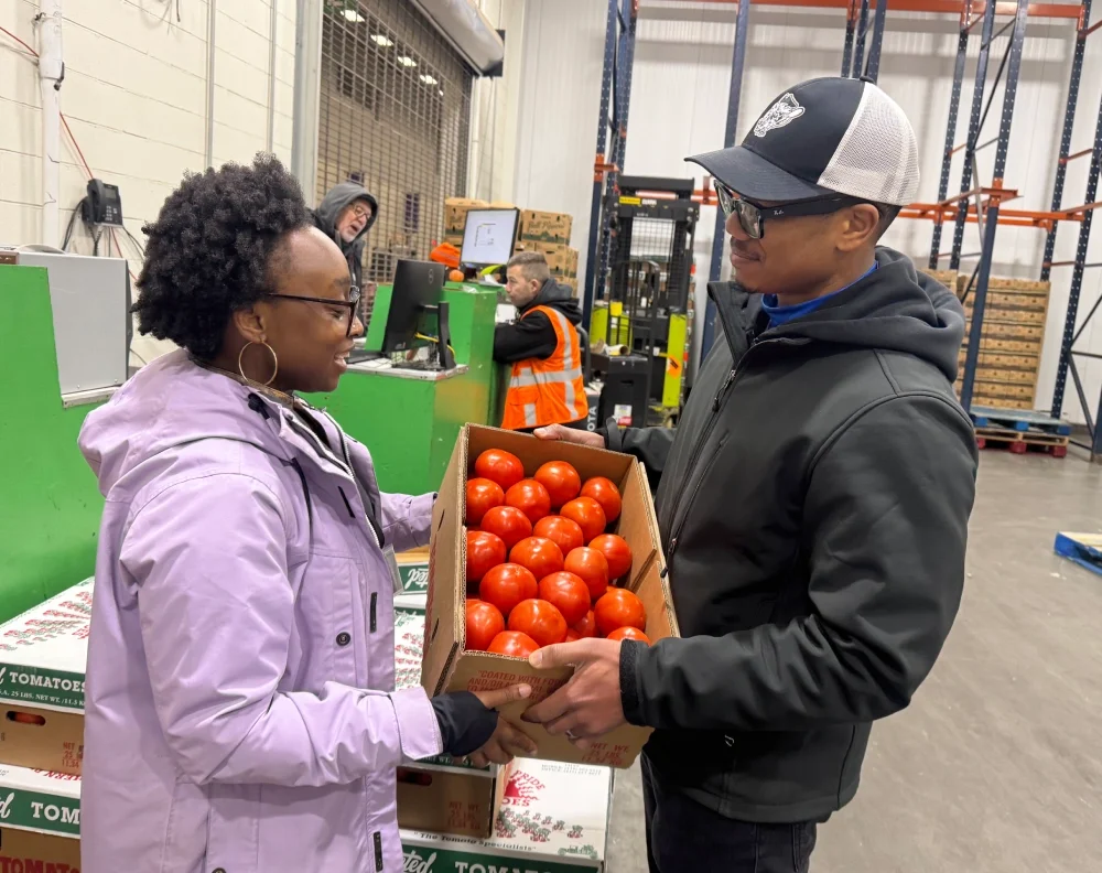 A donor at the Philadelphia produce market donates a case of tomatoes for the weekly food distribution to a volunteer