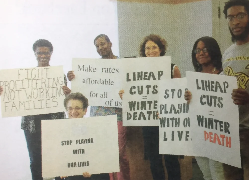 ESWA volunteers and members hold signs opposing utility policies, with slogans "Stop playing with our lives" and "Make rates affordable for all of us"
