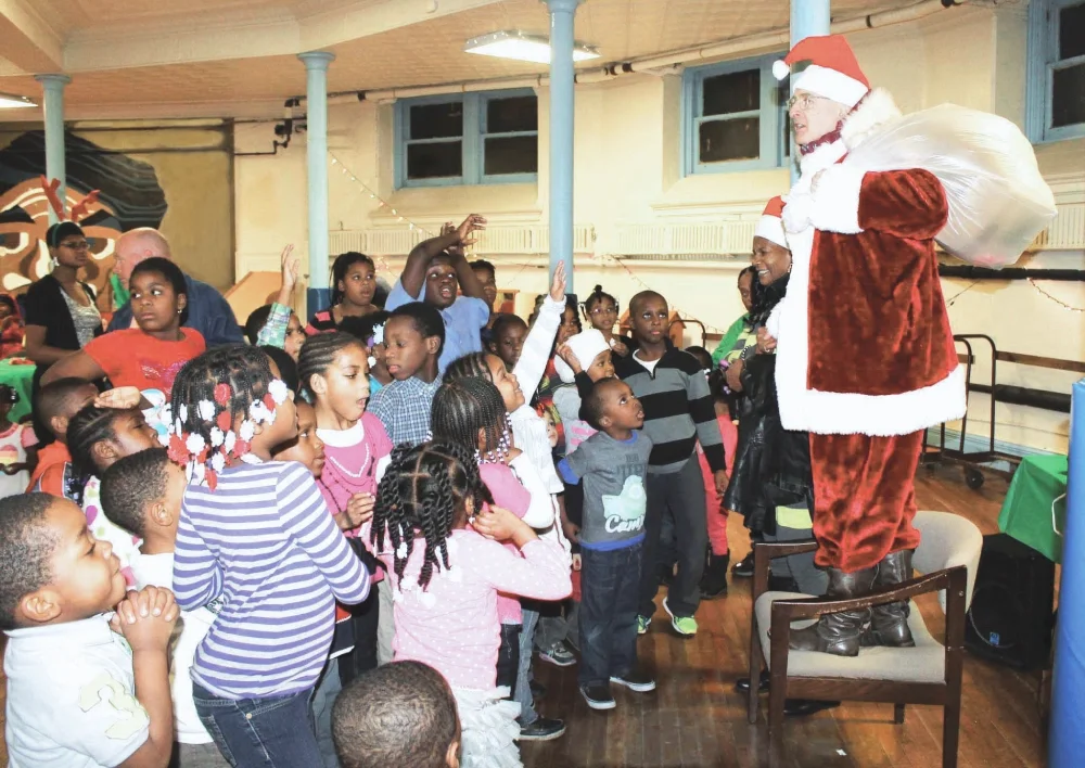 A volunteer Santa Claus stands on a chair to the children at ESWA's Holiday Family Party