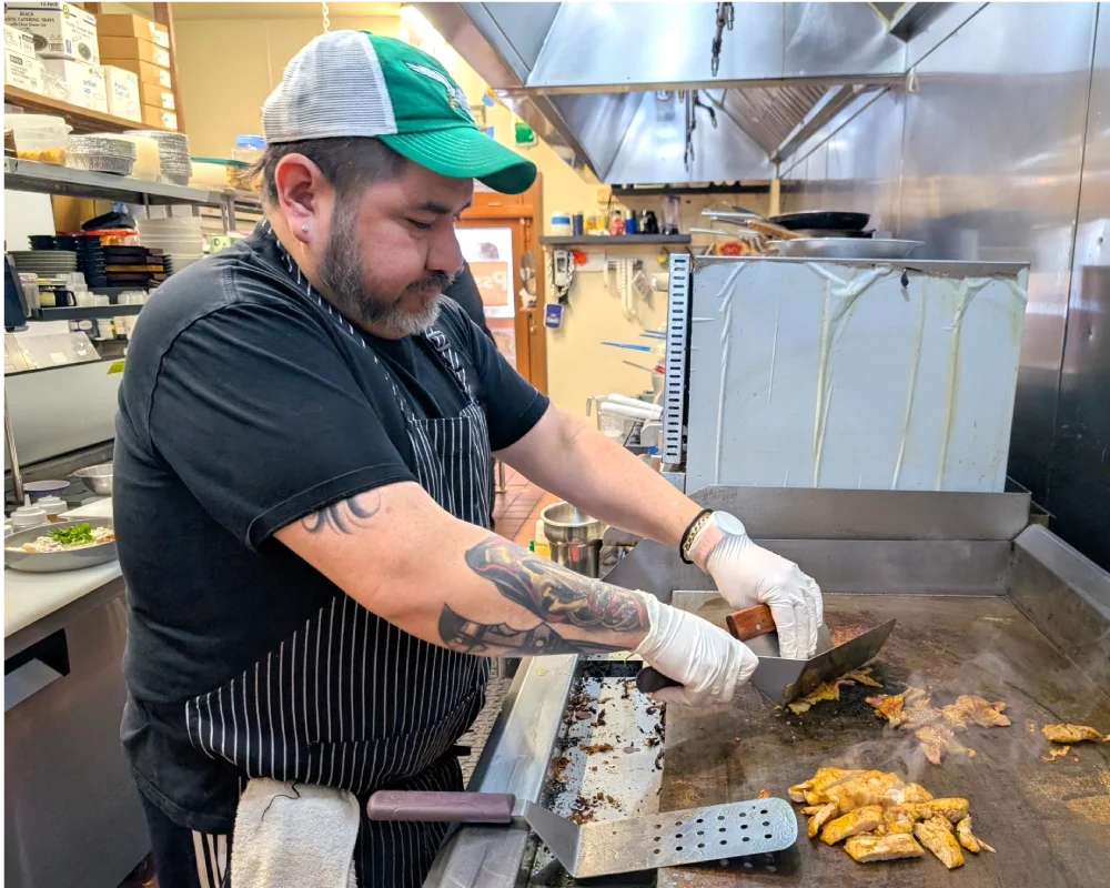 A restaurant cook preparing food on a grill in the kitchen.