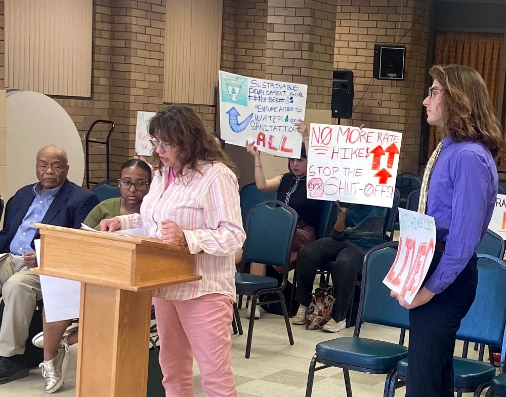 ESWA members speak at a Water Dept hearing against rate increases holding signs that say "No more rate hikes"