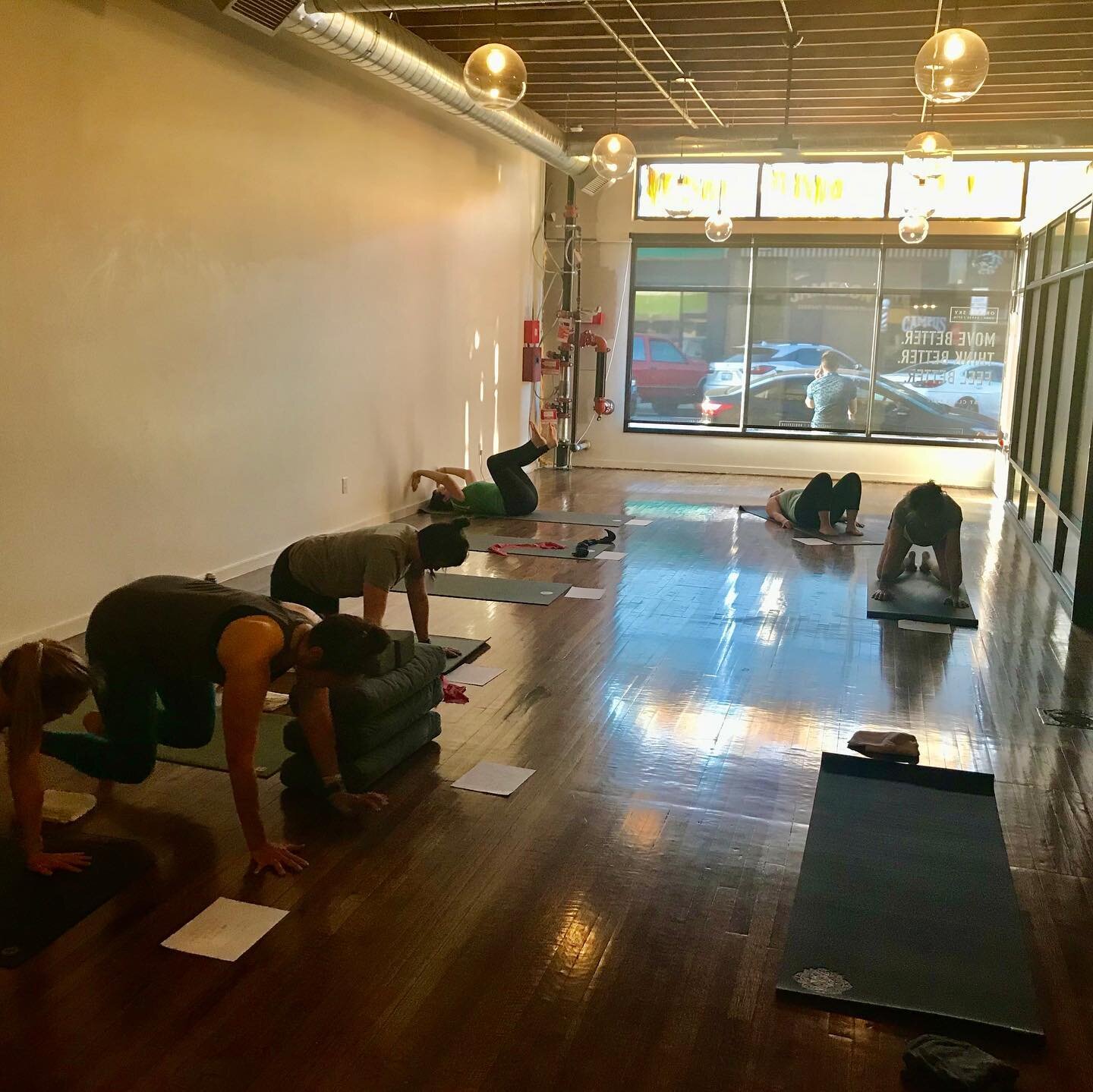 People practicing yoga in a studio with large windows and wooden floors.