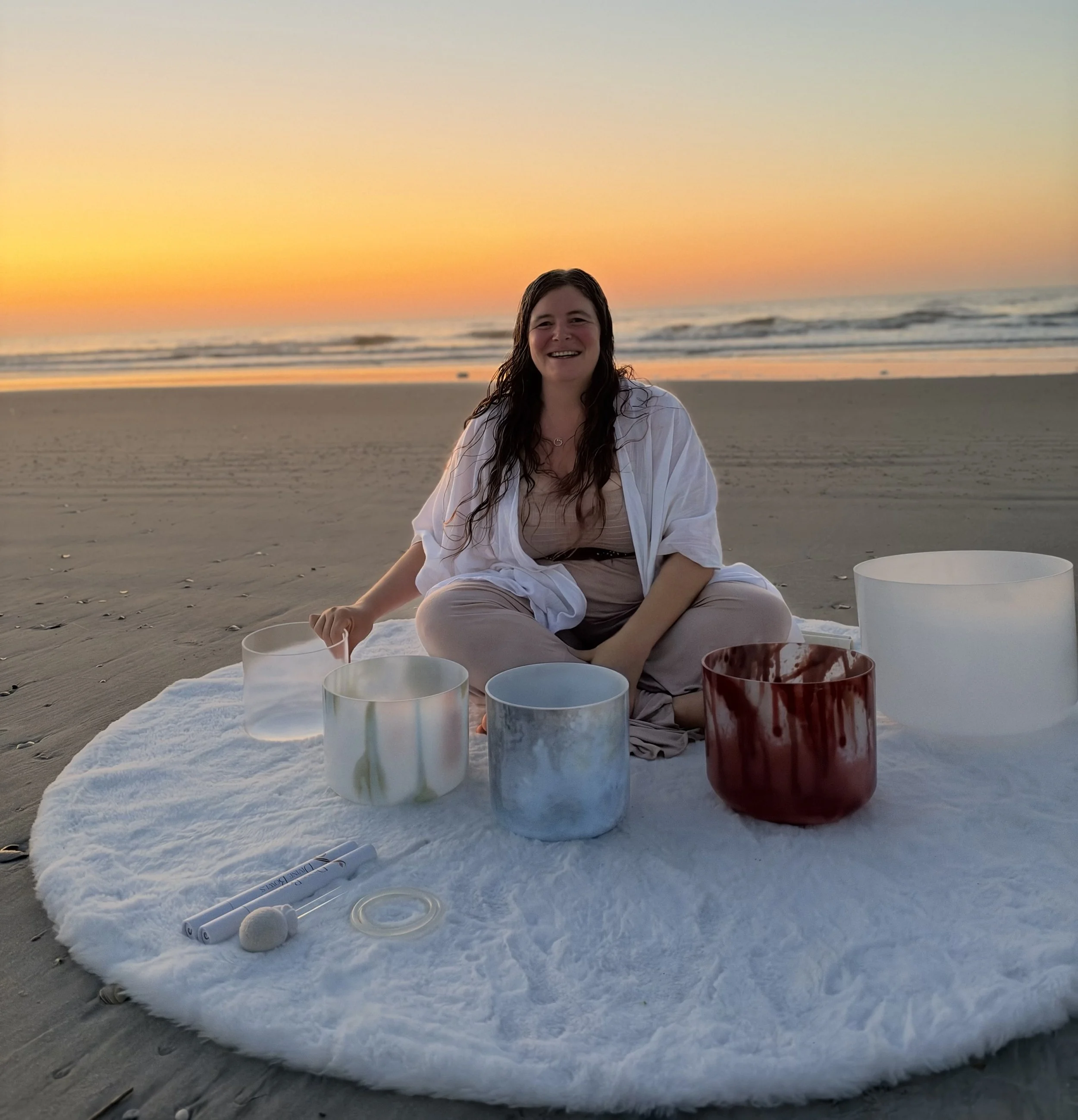 Megan Ann Walker seated with Divine Bowls crystal singing bowls on an Ocean City, NJ beach at sunrise.