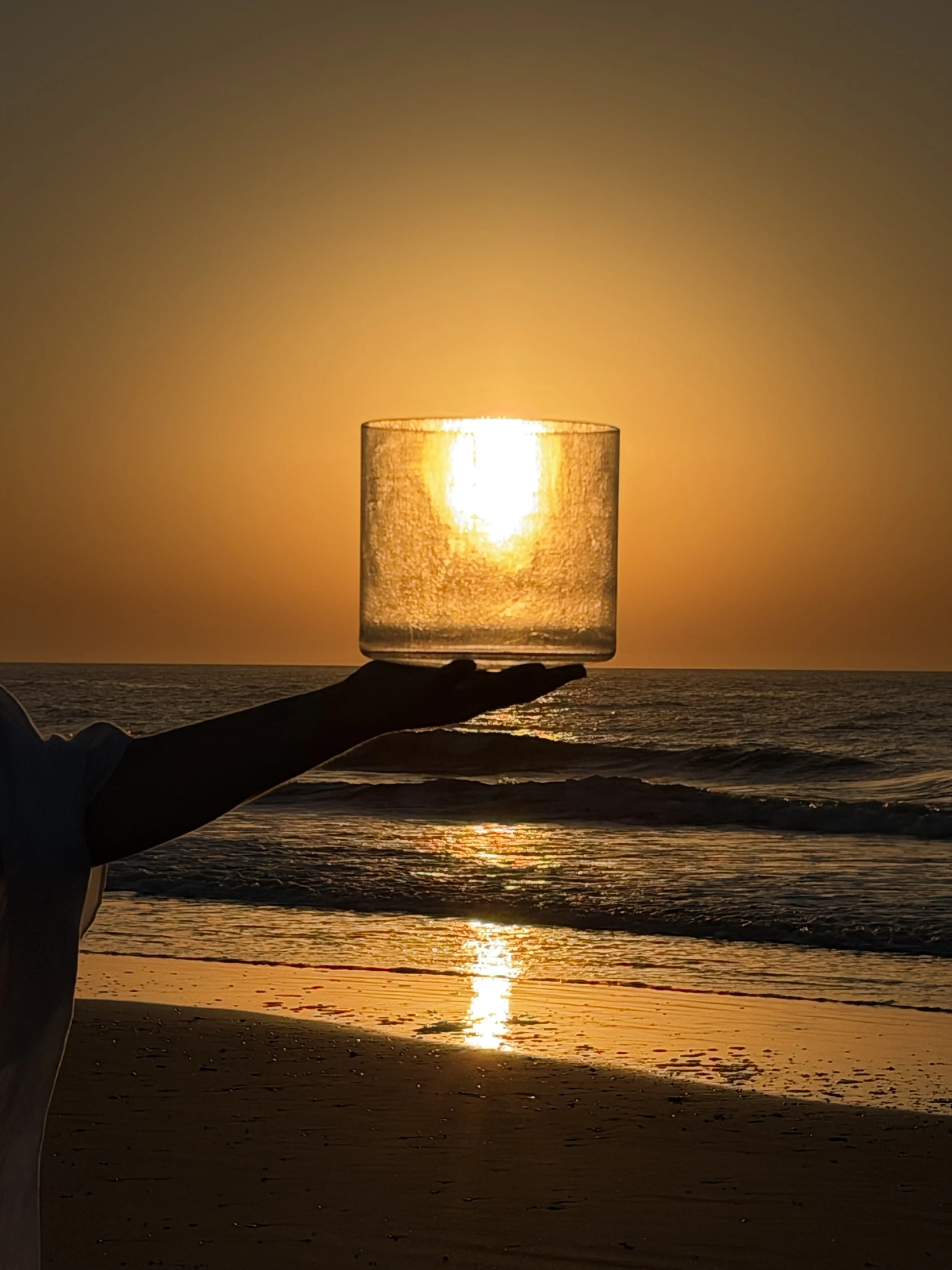 Clear quartz singing bowl held against the rising sun over the ocean.