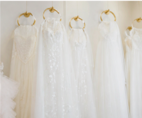 Several white wedding dresses hanging on gold hooks.