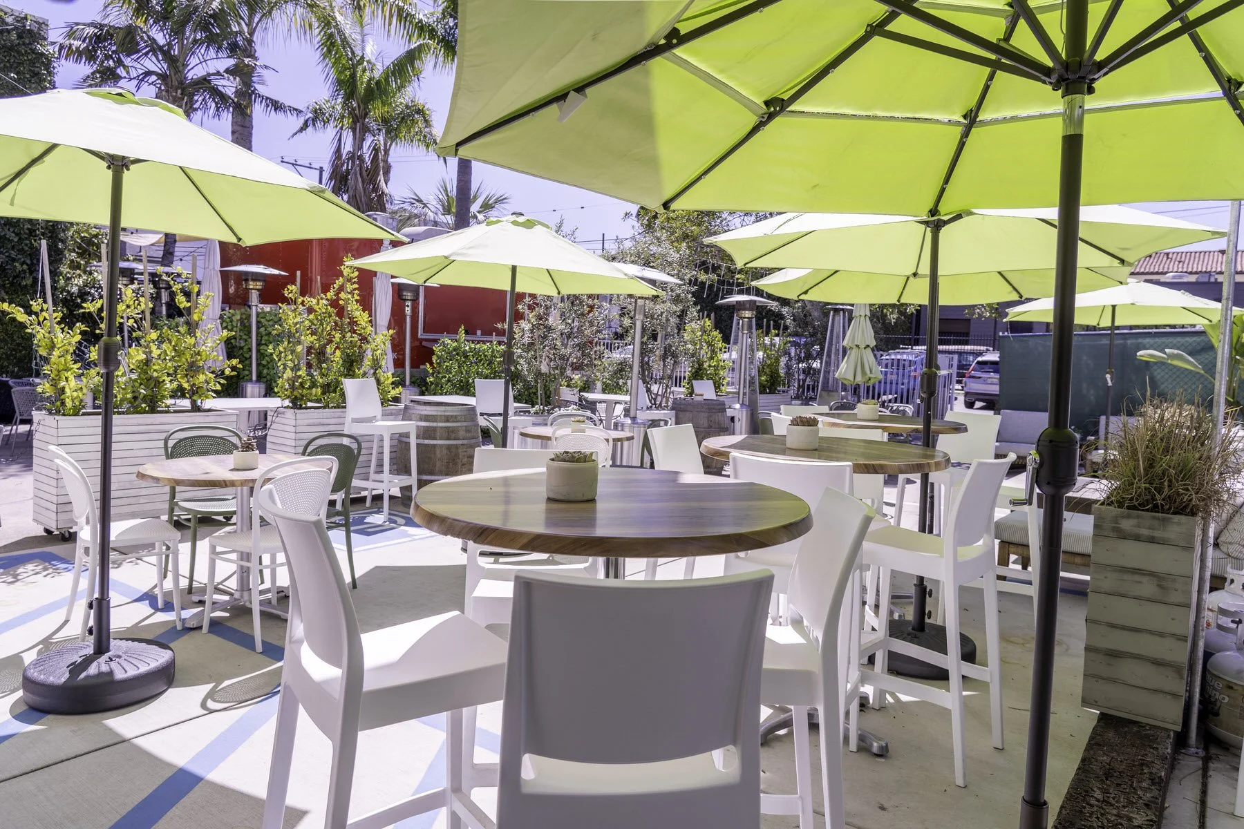 Outdoor patio with white and green chairs, round wooden tables, yellow umbrellas, and potted plants on a sunny day