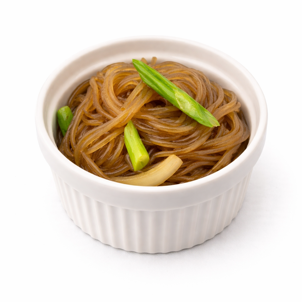 Bowl of cooked brown rice noodles with green onion garnish on white background