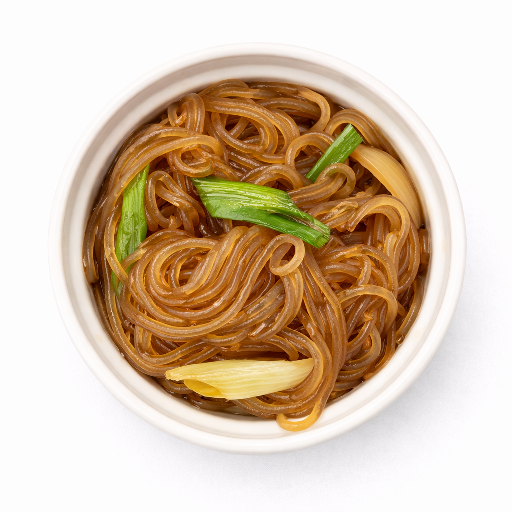 A white bowl filled with cooked brown ramen noodles garnished with green onions.