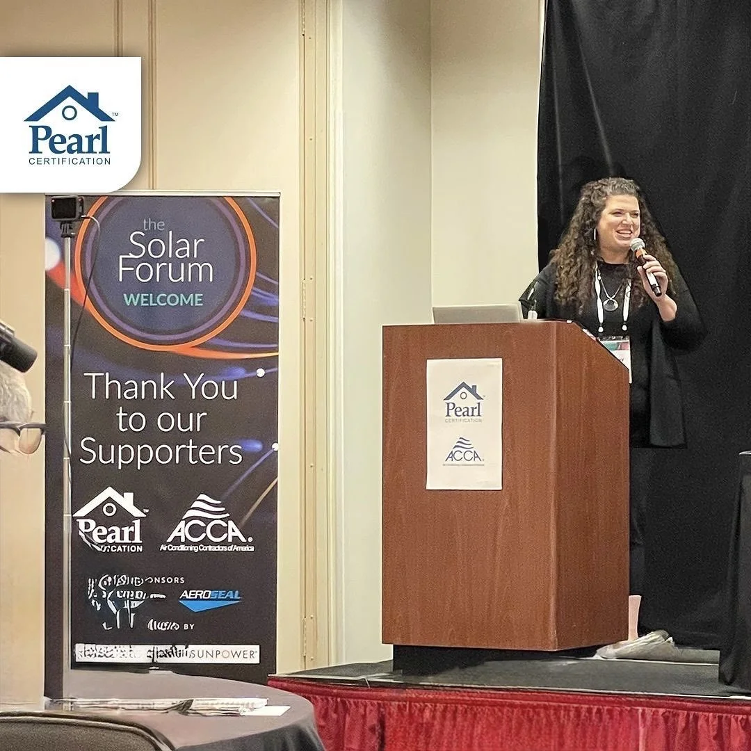 A woman speaking into a microphone at a podium during the Solar Forum. A banner to her left displays greeting and supporter logos, including Pearl Certification and ACCA, with a thank you message to supporters.