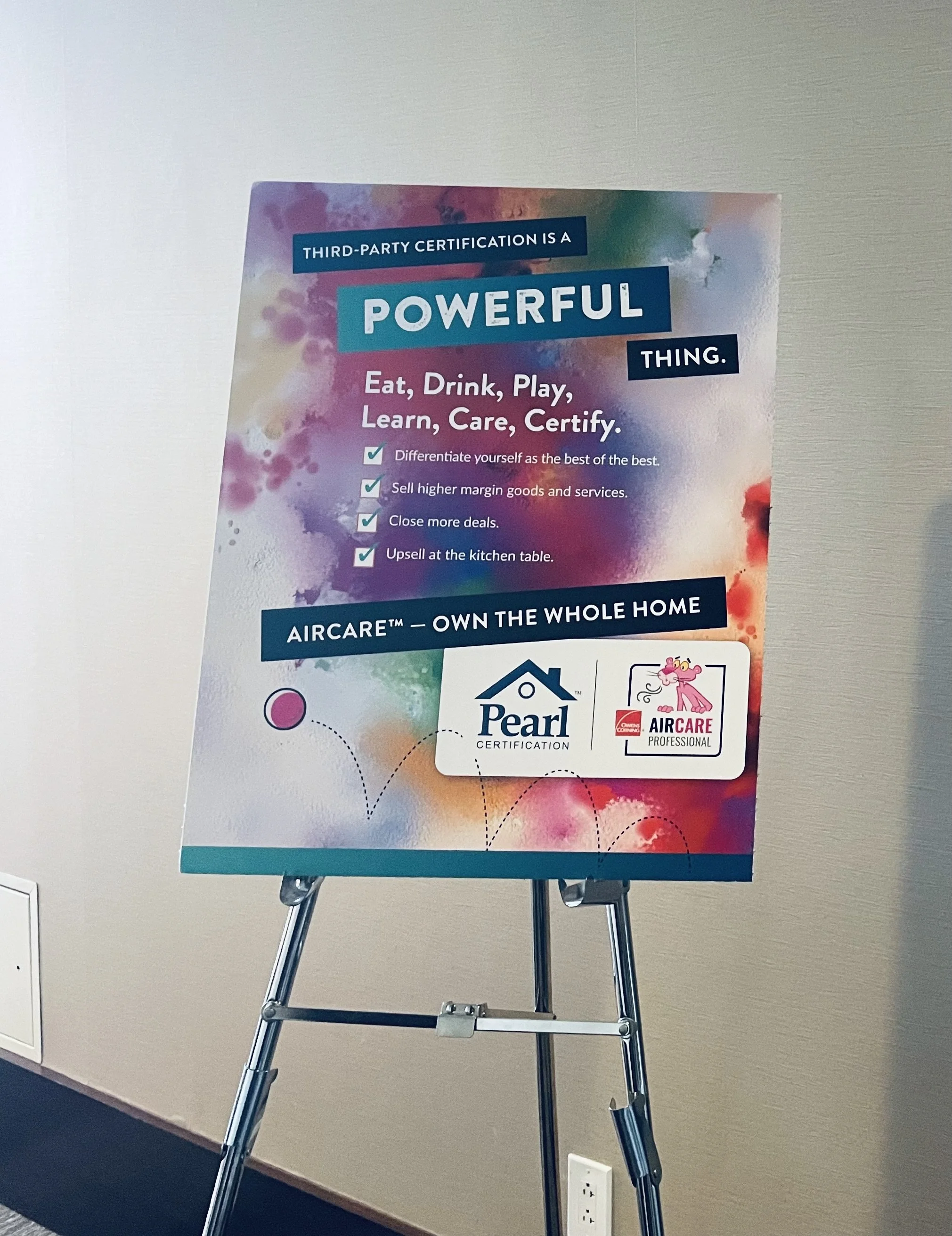 Colorful poster on an easel promoting third-party certification for the Aircare™ system, with the Pearl Certification logo and Aircare professional logo, featuring text about education, certification, and home care.