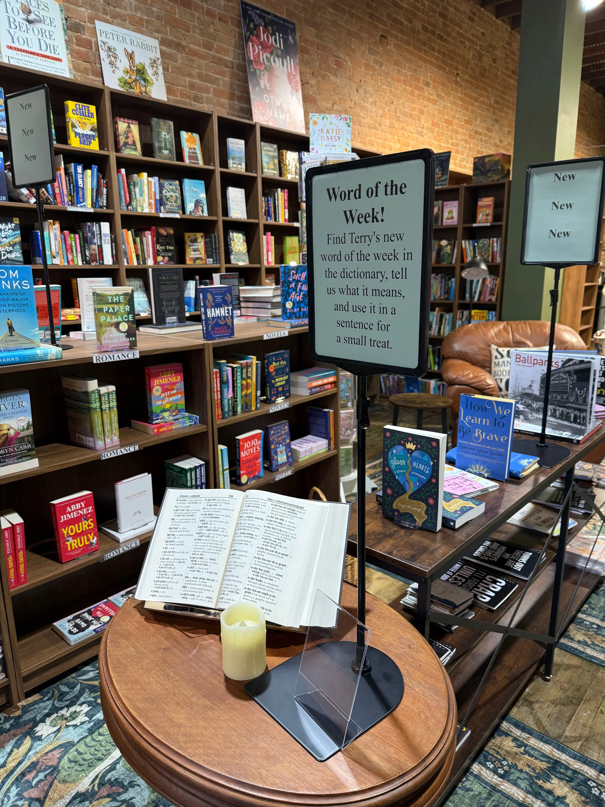 A display in a bookstore featuring books and signs, with a wooden table holding a Bible and a candle, and shelves filled with various books in the background.