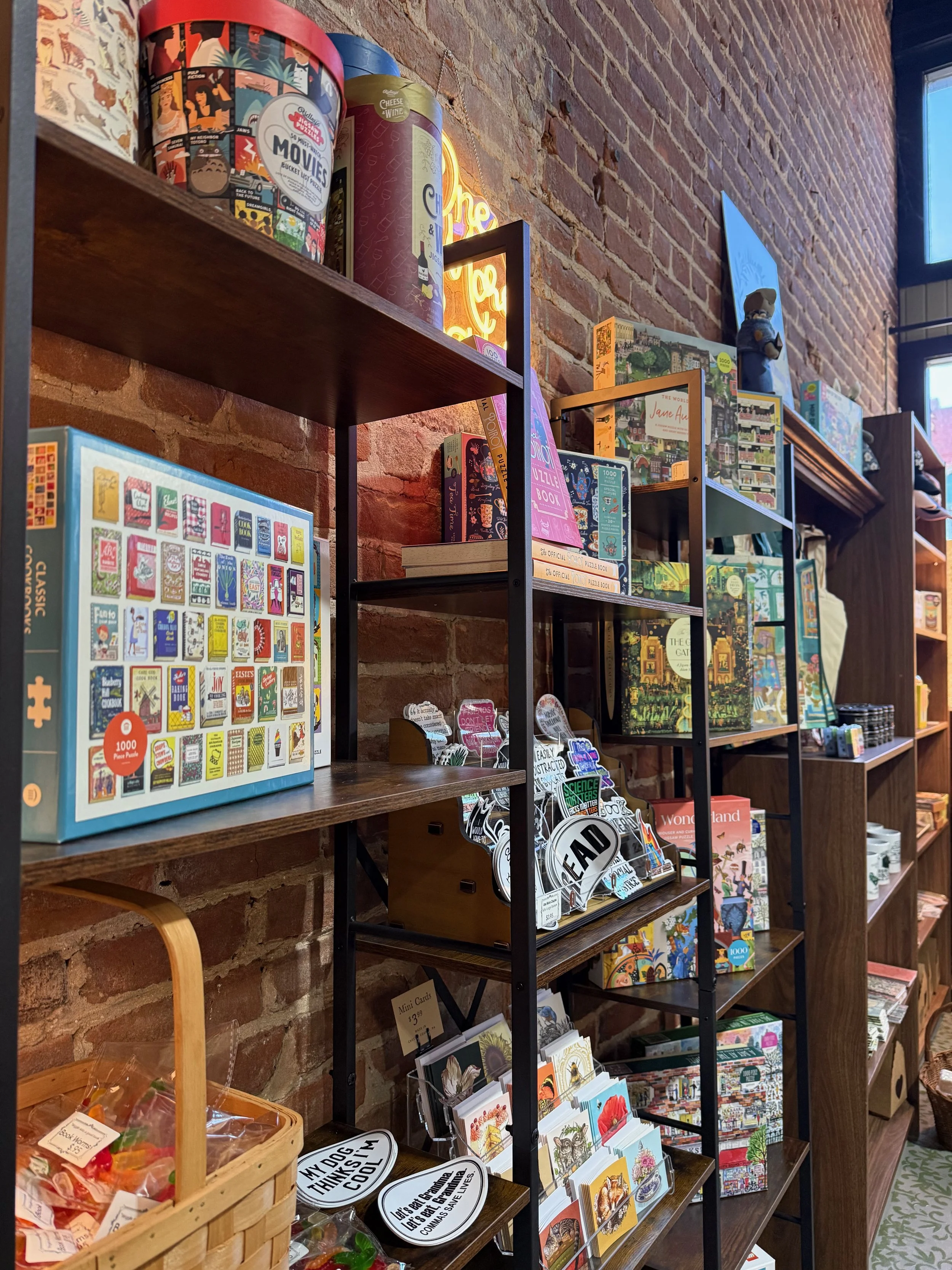 Books and puzzles on display shelves in a bookstore with a brick wall background.
