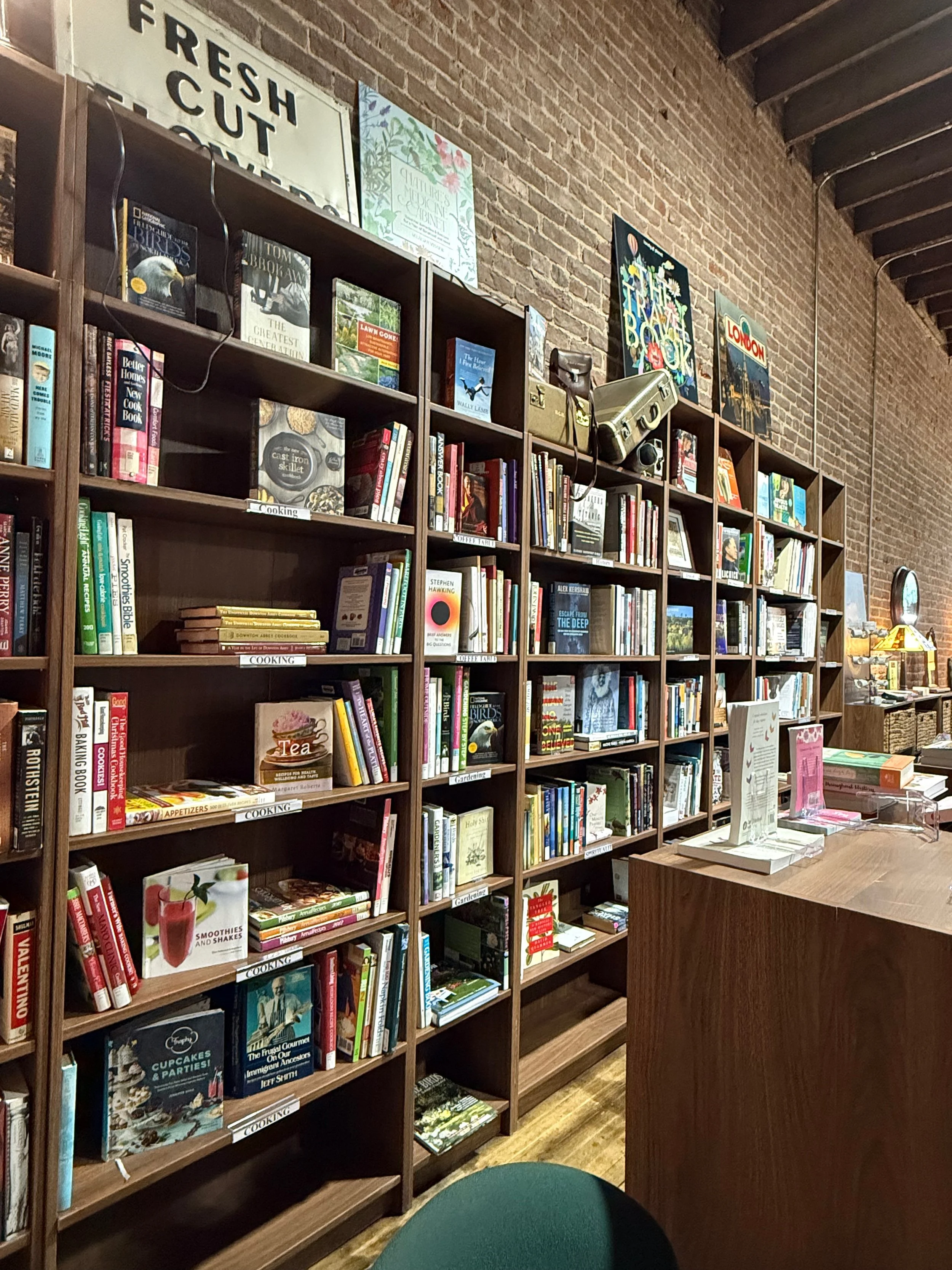 Bookshelves filled with books in a bookstore with a brick wall and a wooden ceiling.