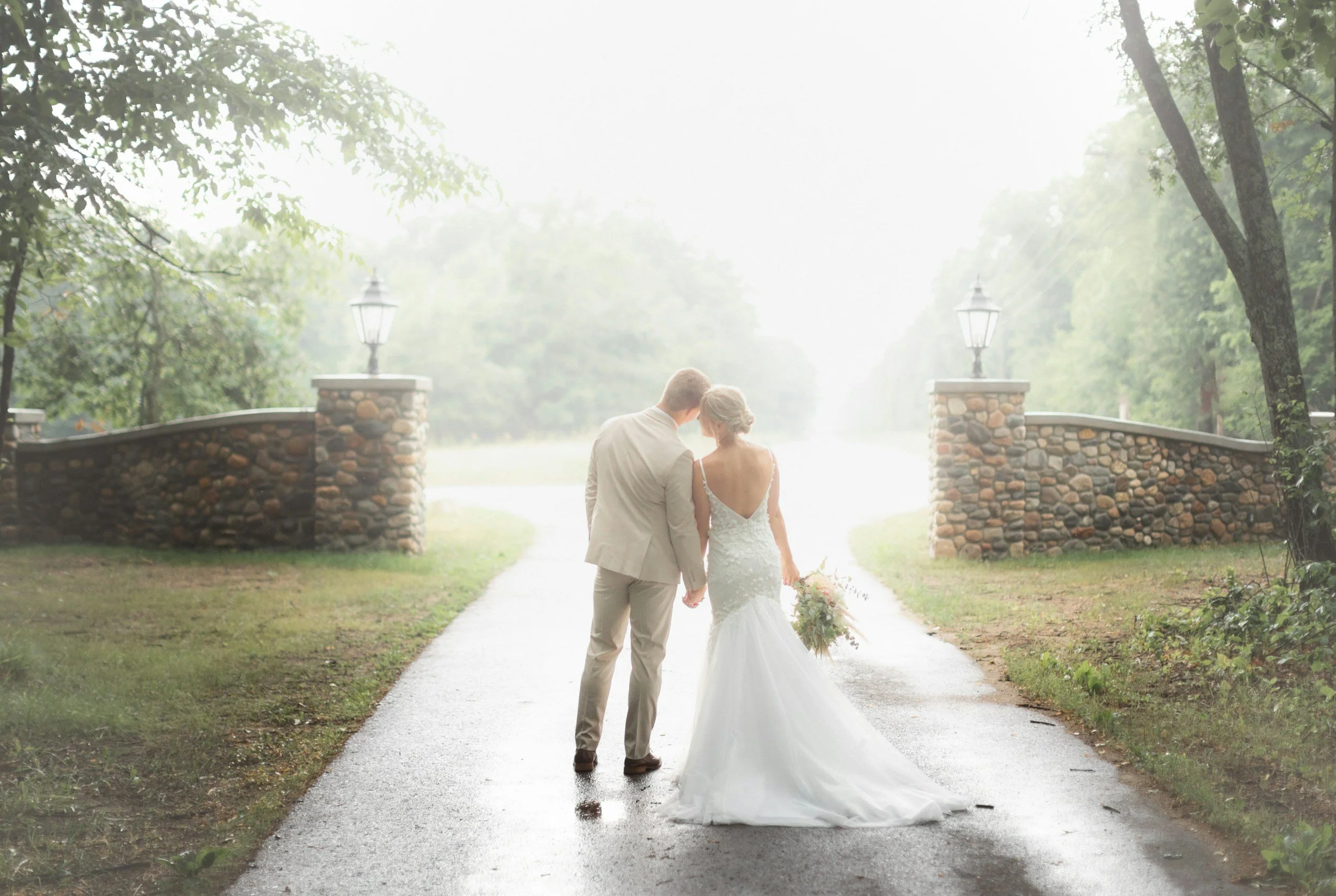 A bride and groom standing outside a venue walking along with a white dress, cream suit and flowers