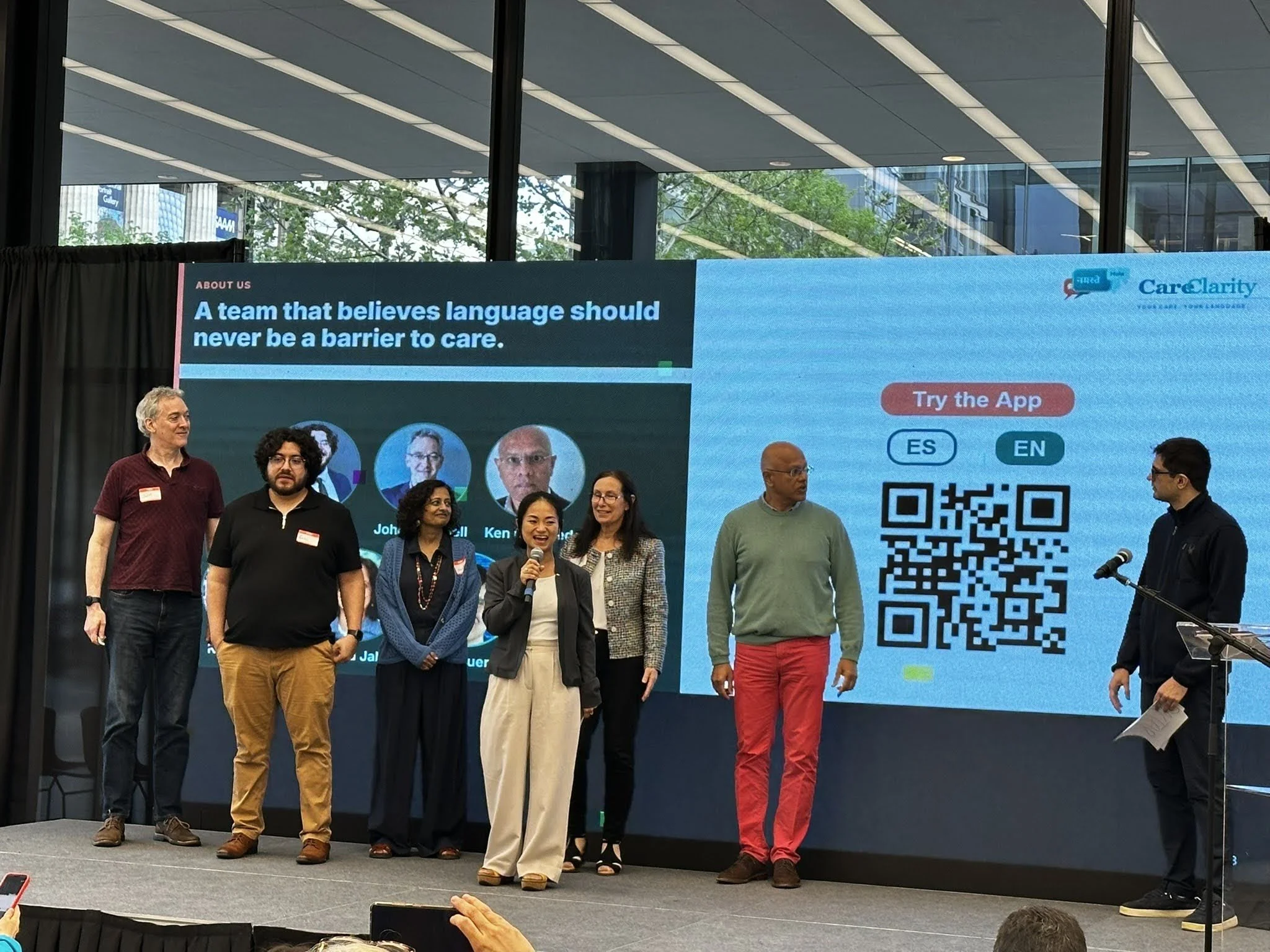 John D. Cornwell, Eric Rivera, Madhu Jalan, Kim Nyugen,‍ ‍Christine Whalen, Ken Figueredo, and Samuel Figueredo presenting their CareClarity app on stage..