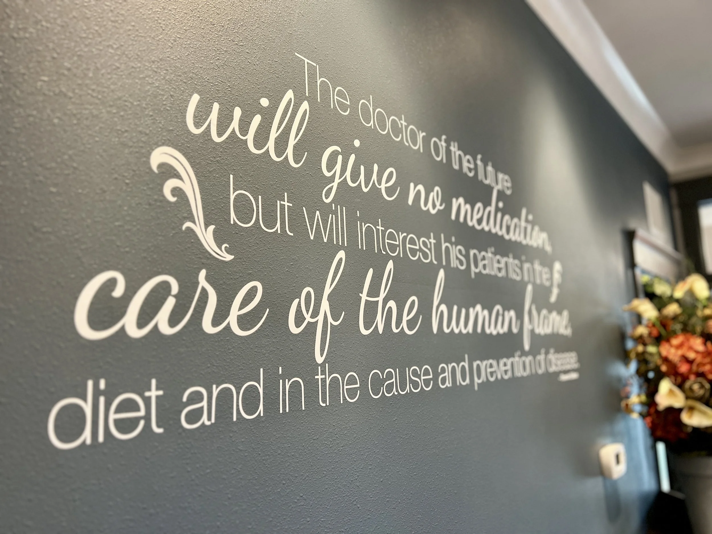Decorative wall with a quote about medicine and healthcare, partially visible, with a flower arrangement on the side.