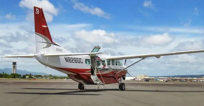 Turboprop airplane on tarmac with stairs attached for boarding, under partly cloudy sky.