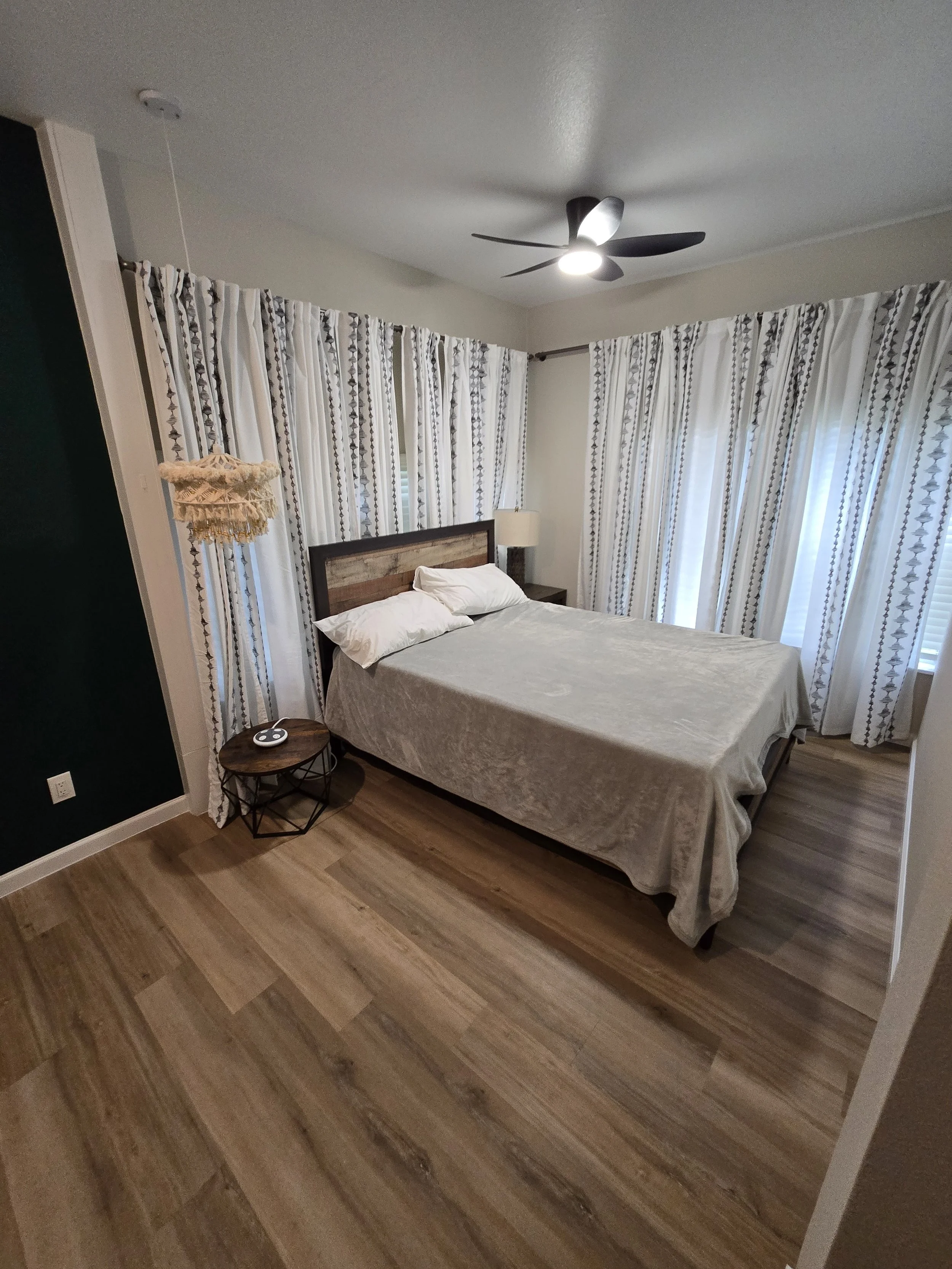 A bedroom with a bed, nightstand, and ceiling fan, with patterned curtains covering windows.